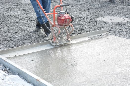 A construction worker operates a power trowel to smooth freshly poured concrete on a construction site.